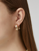 Gold hoop earrings worn by a person with long brown hair on a neutral background