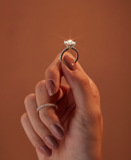 Hand holding a diamond ring against a warm brown background